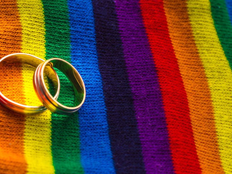 Two wedding rings on a vibrant rainbow-striped fabric, symbolizing LGBTQ+ pride and unity.