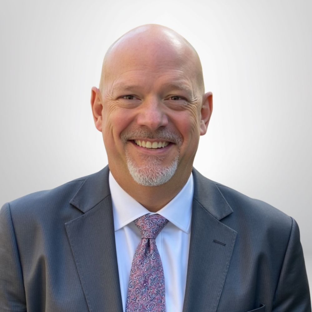 Smiling man in a suit and tie against a neutral background.