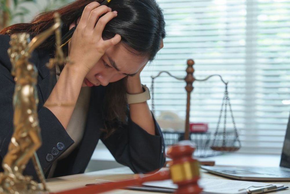Stressed lawyer in office with legal scales and gavel visible, holding head in frustration.