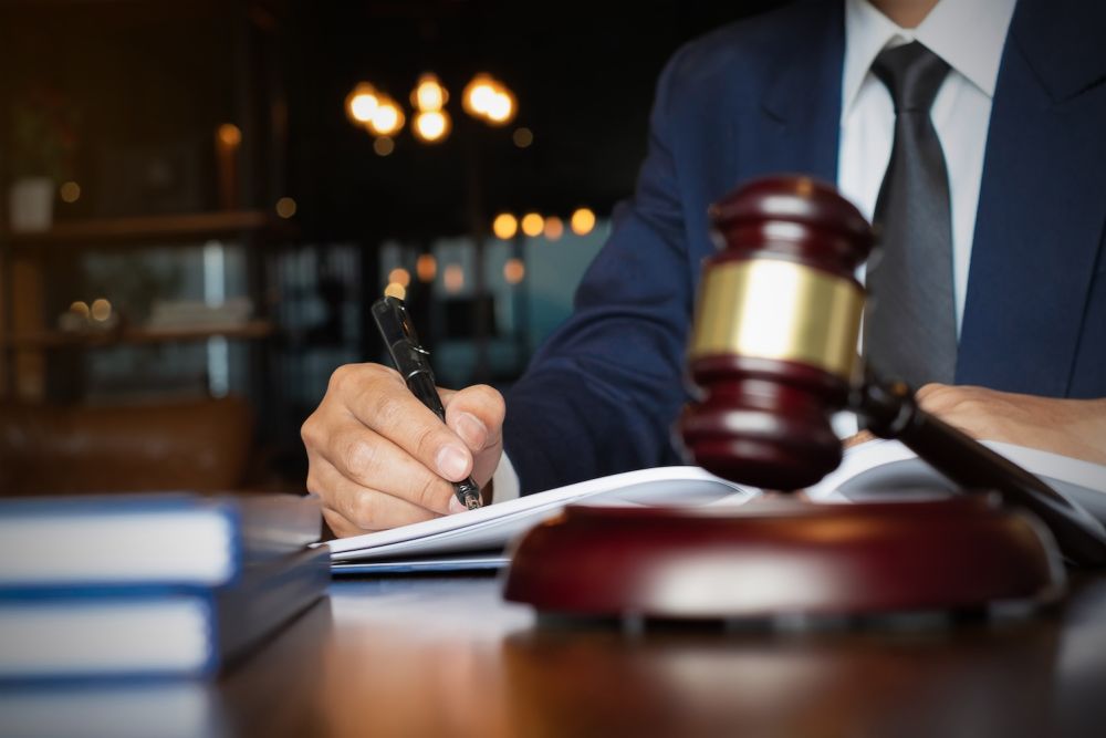 Lawyer writing at desk with gavel in foreground, symbolizing legal work and justice.