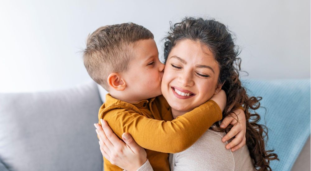 Mother and son sharing a joyful hug and kiss on a cozy couch, expressing love and happiness.
