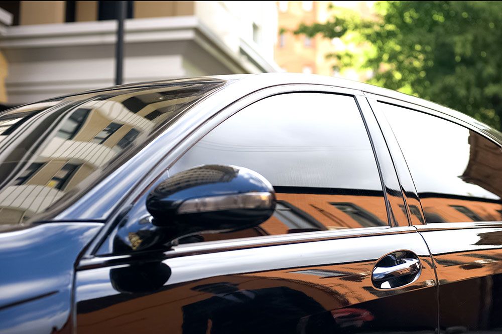 Sleek black car with tinted windows reflecting a cityscape, emphasizing luxury and urban lifestyle.