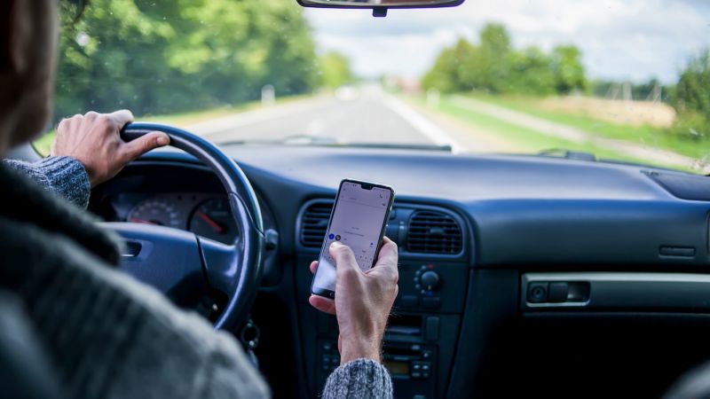 Driver using a smartphone while driving on a road; distracted driving safety concern.