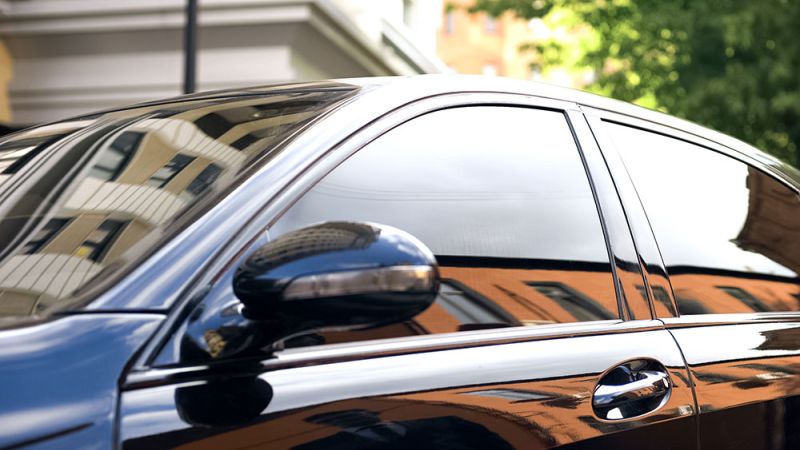 Sleek black car with tinted windows reflecting a cityscape, emphasizing luxury and urban lifestyle.