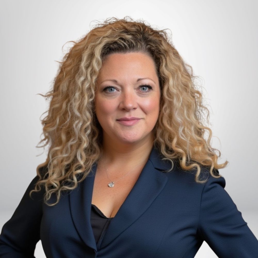 Confident woman with curly hair in business attire, smiling at the camera against a neutral background.