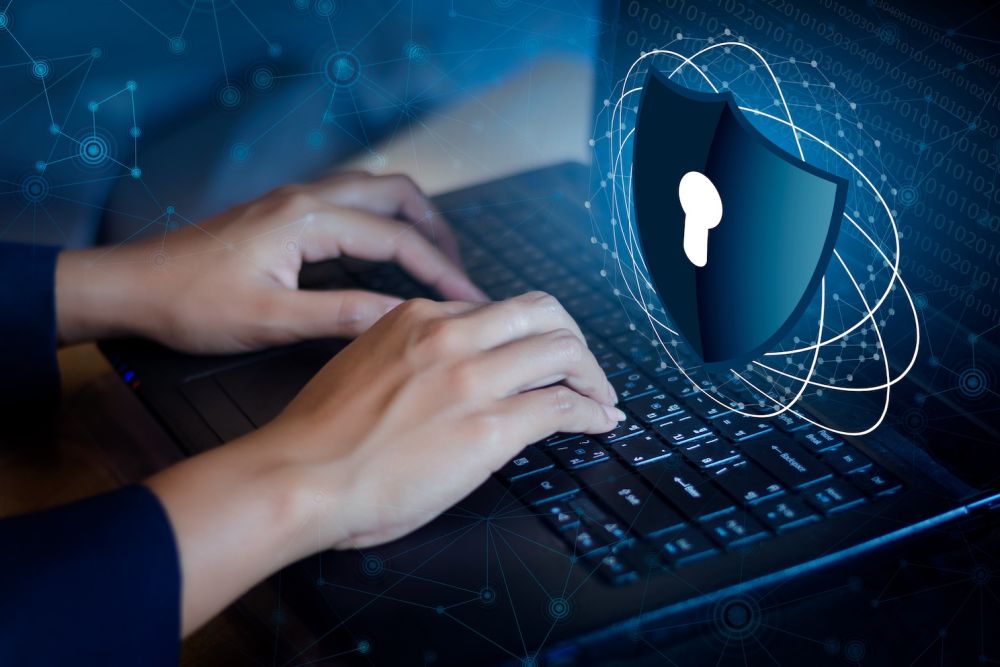 Hands typing on laptop keyboard with digital security shield overlay, representing cybersecurity and data protection.