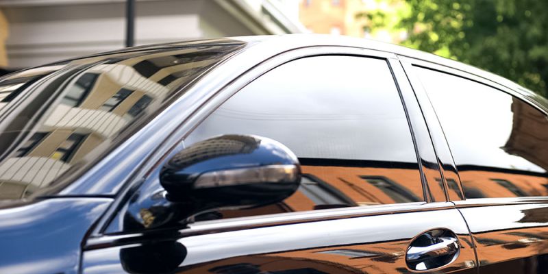 Sleek black car with tinted windows reflecting a cityscape, emphasizing luxury and urban lifestyle.