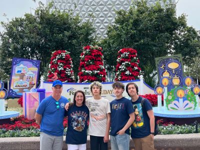 Family posing at Epcot Center during holiday festival, standing in front of Spaceship Earth and festive decorations.