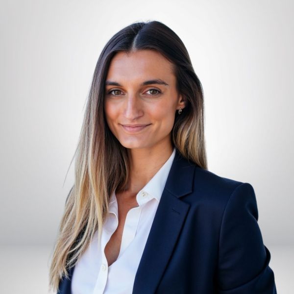 Professional woman in navy blazer smiling against neutral background.