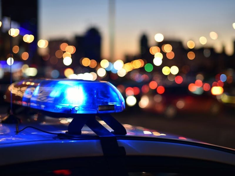 Police car with flashing blue lights in city traffic at dusk, blurred background with colorful bokeh.