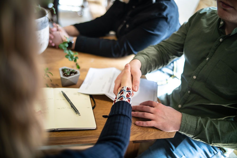 Handshake at a meeting table with notebook and documents, symbolizing business agreement or partnership.