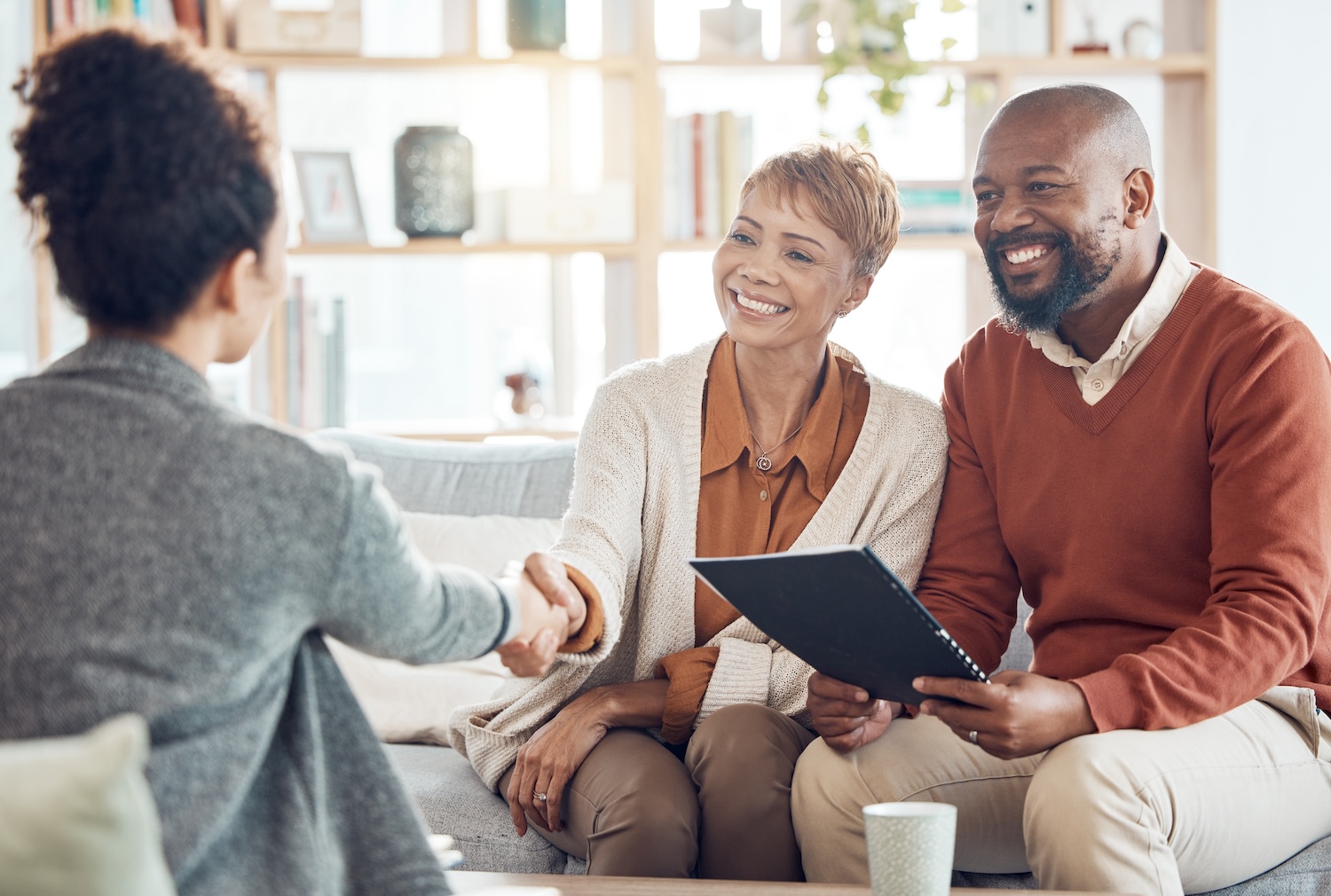 Smiling couple meeting with professional advisor, shaking hands in a cozy office setting.
