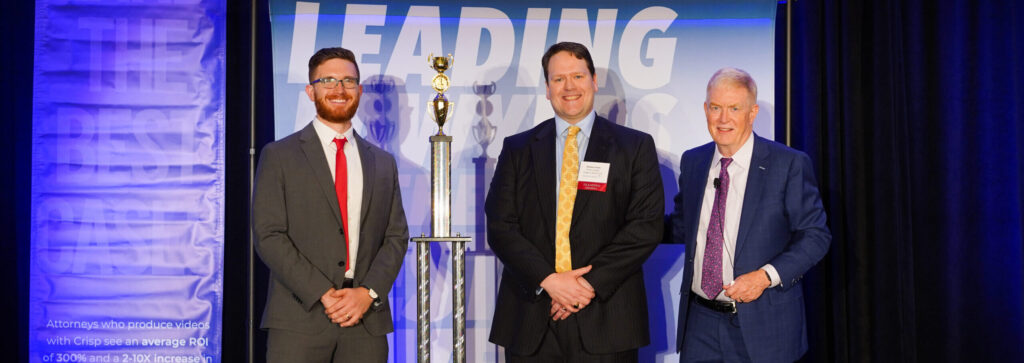 Three Men in Suits Pose with a Tall Trophy at a Business Event Against a Blue Backdrop