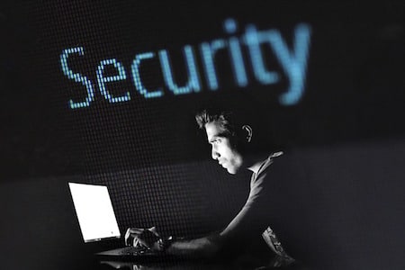 Person Typing on Laptop in Dim Light Large 'Security' text in background, representing cybersecurity concepts.