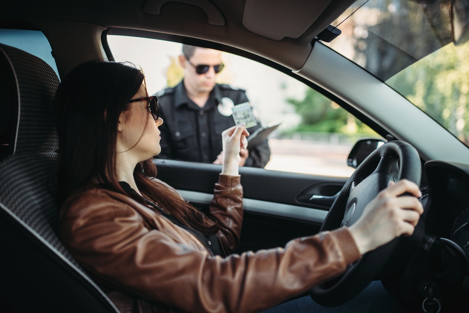 Woman driver handing license to police officer during a traffic stop.