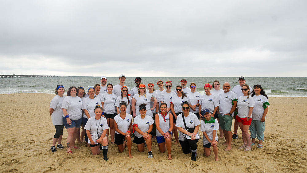 Group of People Wearing Matching Shirts on a Beach with Ocean in Background Under a Cloudy Sky